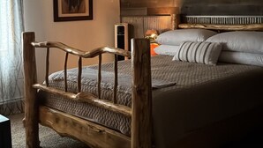 A bedroom with a wooden bed frame, a ceiling fan, a wall-mounted heater, and a framed picture on the wall. - Mountain Modern Condo (Cody)