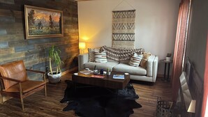 A cozy living room with a wooden wall, a sofa, a coffee table, a leather chair, and a hanging tapestry. - Mountain Modern Condo (Cody)