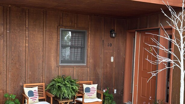 A wooden building with a balcony, two wooden chairs with American flag cushions, and a potted plant. - Mountain Modern Condo (Cody)