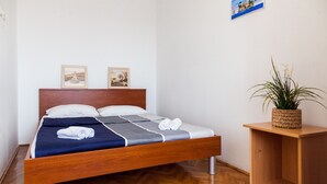 Ein ordentlich bezogenes Bett mit einem hölzernen Kopfteil, ein kleiner Nachttisch mit einer Pflanze und zwei gerahmte Bilder an der Wand.