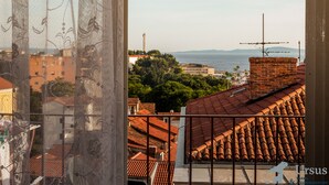 Blick aus einem Fenster mit einer dekorativen Gardine auf eine Stadtansicht mit roten Ziegeldächern, ein Backsteingebäude und ein weiter See in der Ferne.