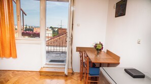 Una habitació amb un terra de fusta en rel d'ocell, una taula de menjador de fusta amb cadirees, un frigorífic petit i una finestra amb vista a edificis i un balcó.