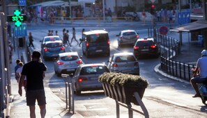 Une rue animée en ville, avec des piétons, des voitures et un panneau vert indiquant une température de 33 °C.