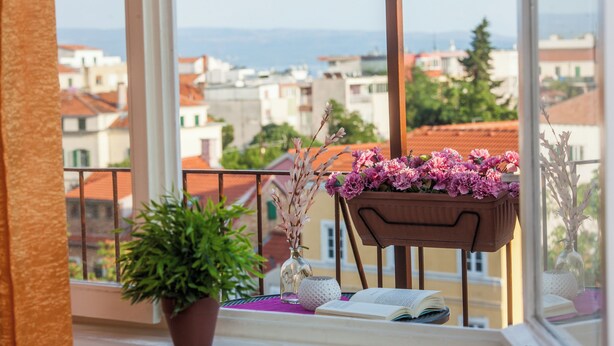 Ein Balkon mit Blumentopf, Blumen in einer Vase, einem Stuhl und einem offenen Buch.