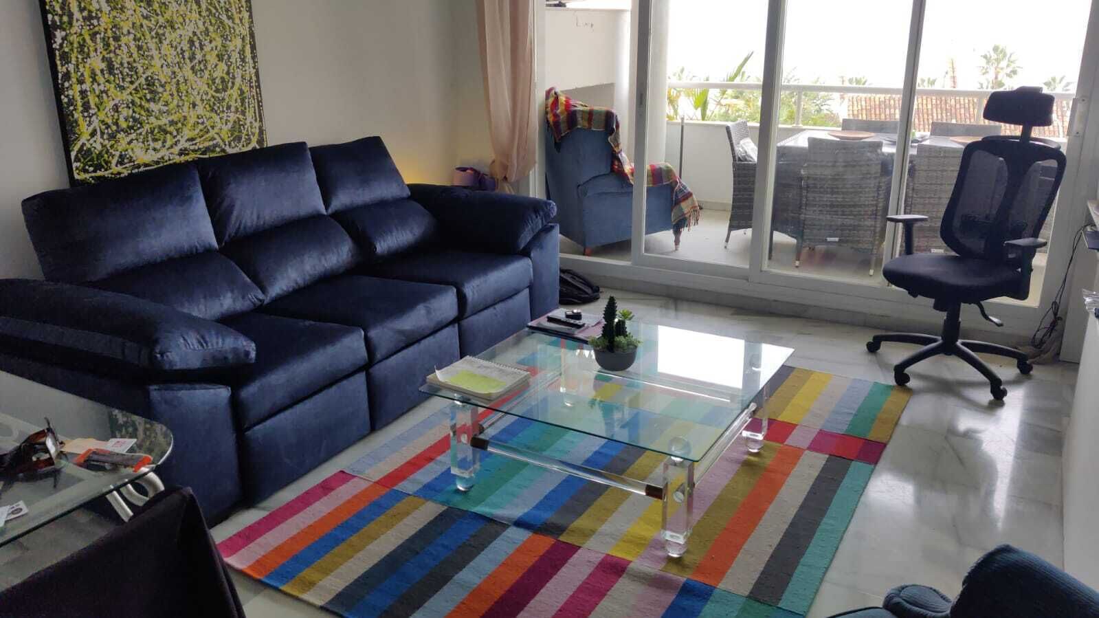 Ein Wohnzimmer mit einem blauen Sofa, einem Glastisch und einem farbenfrohen Streifen Teppich.