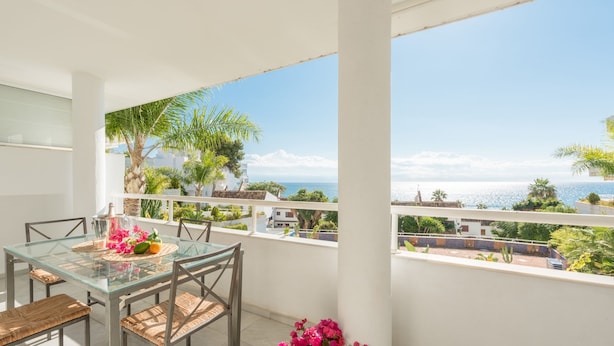 A balcony with a glass table and chairs, a potted plant, and a view of the sea. - Holiday Apartment with seaview (Marbella)