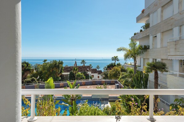 A balcony with a pool, a view of the sea, and a building with balconies and plants.