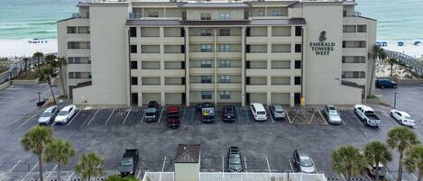 A multi-story hotel with a parking lot, a swimming pool, and a view of the beach.