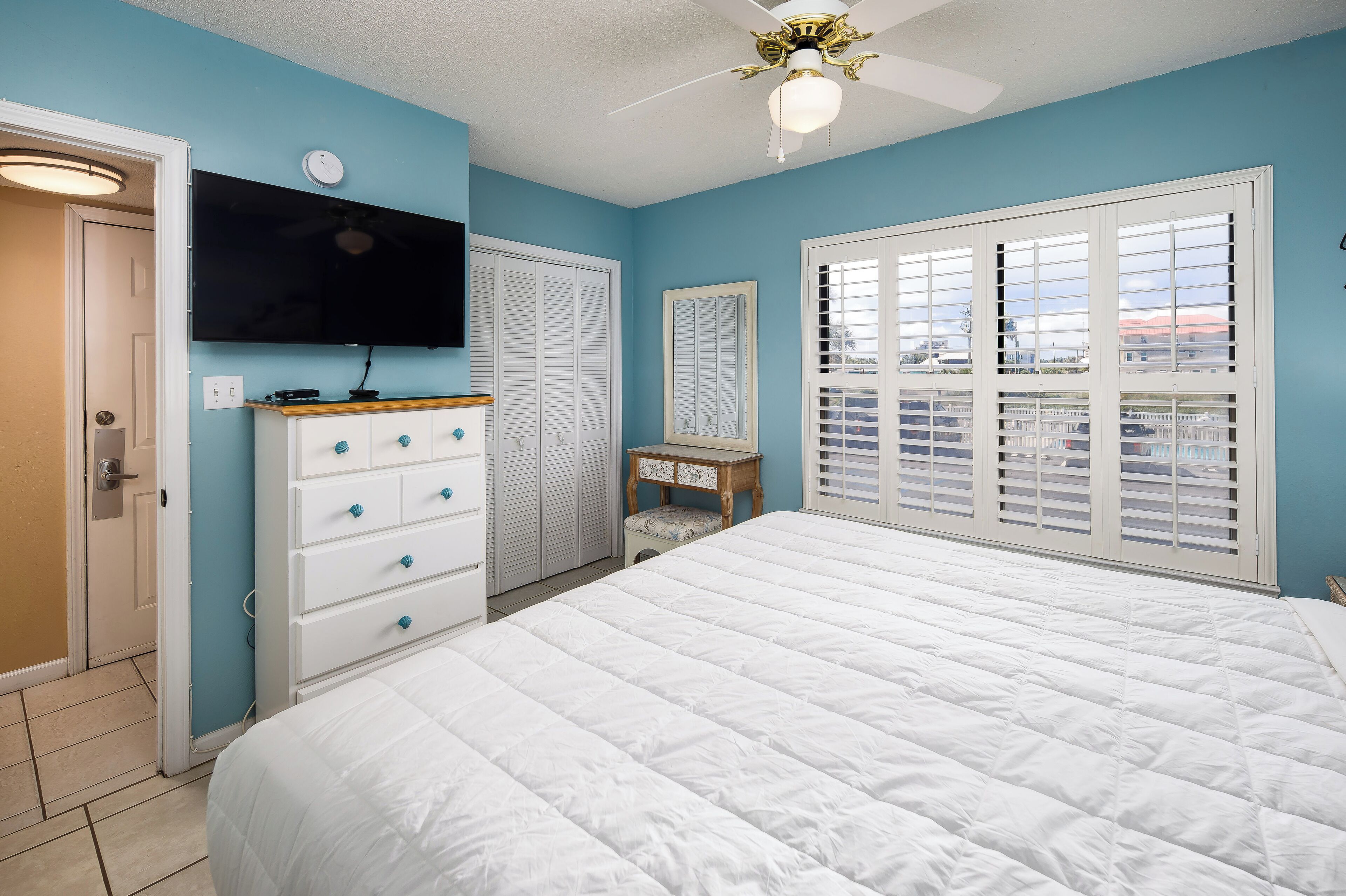 A bedroom with a large bed, a dresser, a television, and a window with blinds.