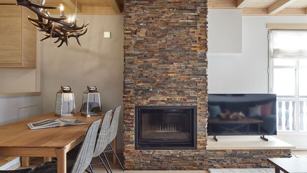 A dining area with a wooden table and chairs, a stone fireplace, and a television on a stand.