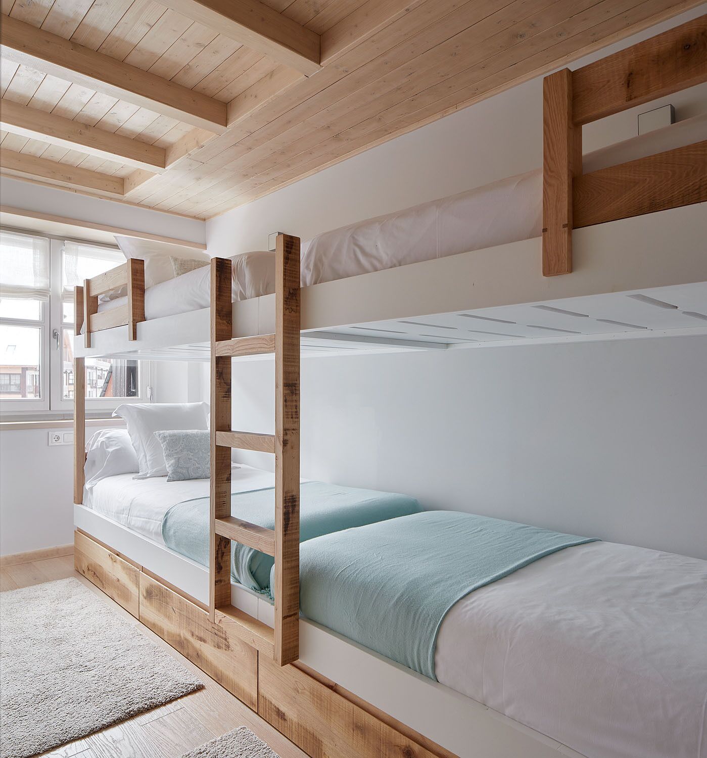 A bunk bed room with wooden beams, white bedding, and a view through a window.