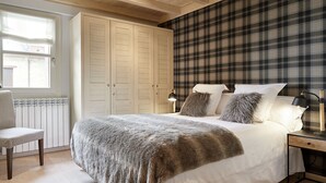 A bedroom with a bed, bedside lamps, a chair, a wardrobe, and a plaid-patterned wall.