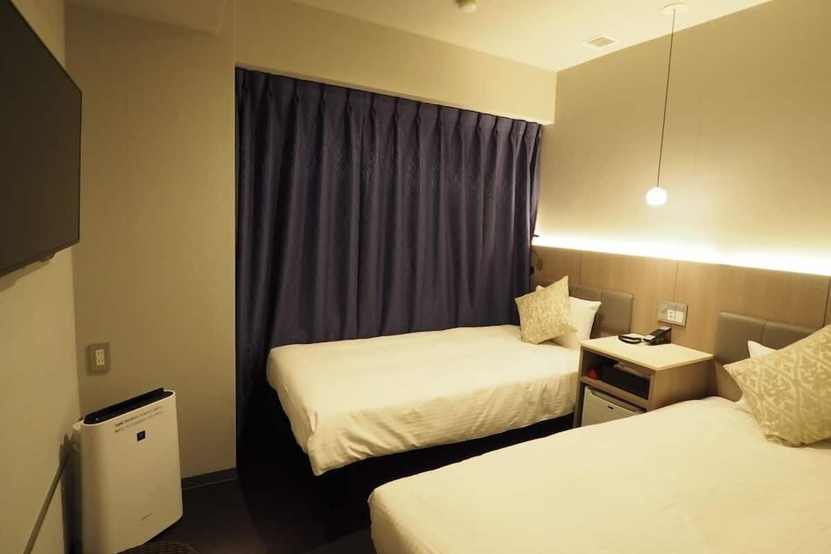 A hotel room with two beds, a TV, a desk, a lamp, and a small heater.