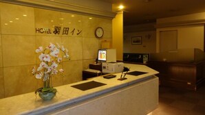A hotel reception desk with a clock, a computer monitor, and a vase of white orchids.