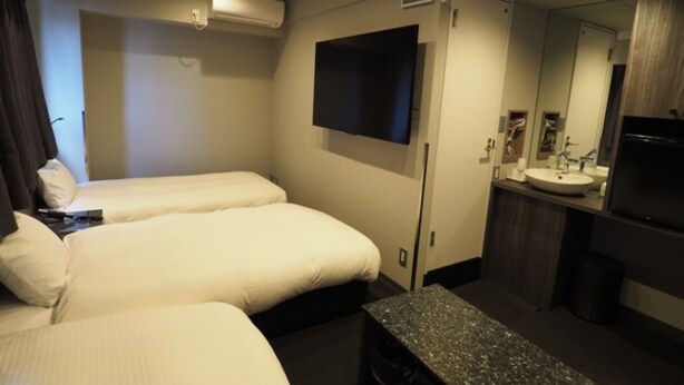 A hotel room with two beds, a flat-screen TV mounted on the wall, a small table, a sink, and a mirror.
