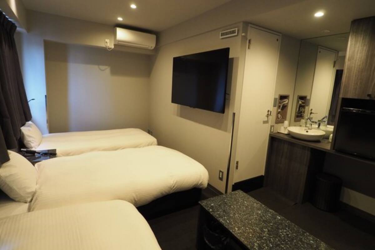 Habitación de hotel con dos camas, un televisor de pantalla plana montado en la pared, una mesita, un lavamanos y un espejo.