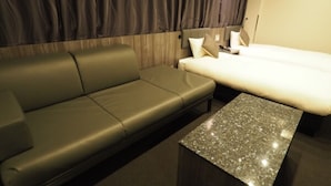 A modern hotel room with a leather sofa, a bed with white bedding, and a granite coffee table.
