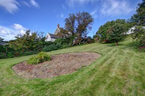 A landscaped garden with a lawn, a circular flower bed, and a house in the background.