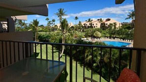 A balcony with a glass table and red patterned cushions, overlooking a swimming pool and lush greenery. - Say Aloha to Island Life! Pool View Suite w/Kitchen Ease, WiFi–Kamaole Sands 6308 (KIHEI)