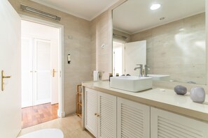 Une salle de bain moderne avec un lavabo blanc, un miroir et des carreaux de couleur beige.