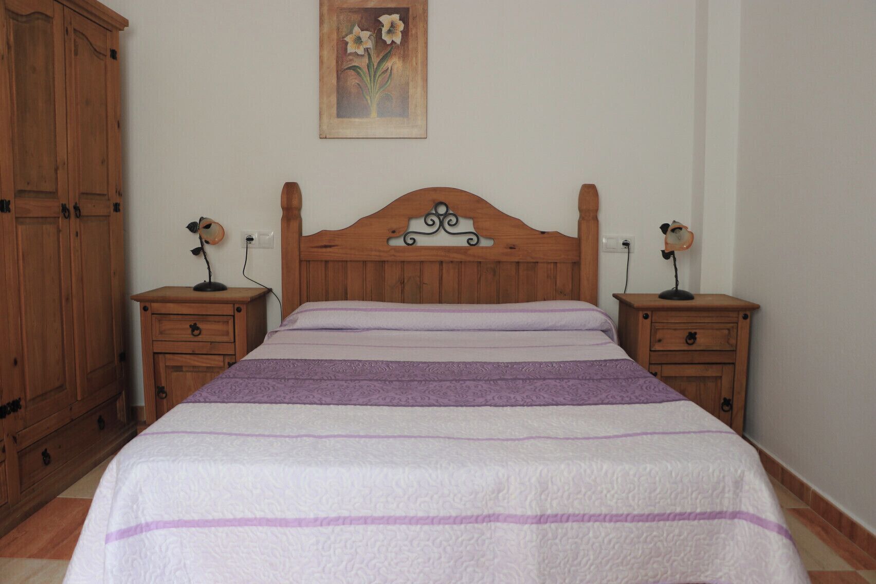 A bedroom with a wooden bed, two nightstands, a wooden wardrobe, and a painting on the wall.