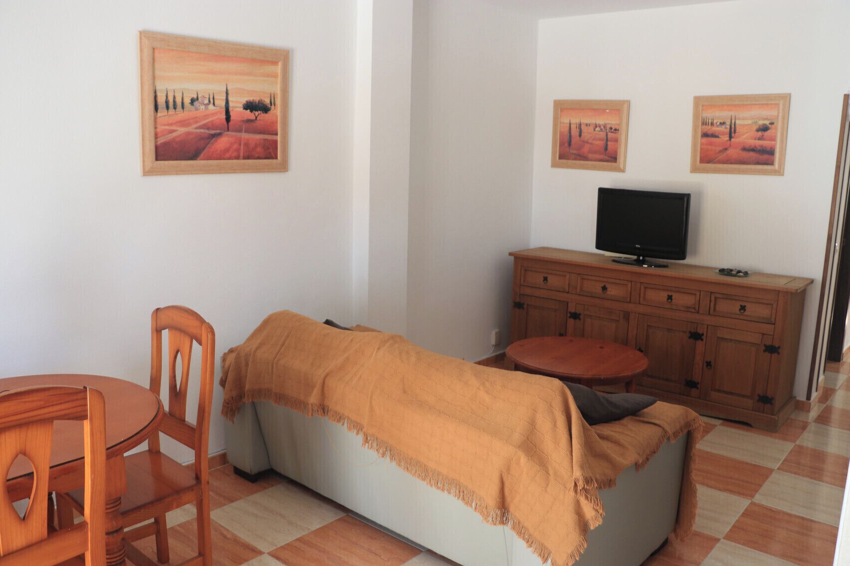 Una habitación amoblada con un sofá, una mesa de comedor de madera, un televisor y dos cuadros en la pared.