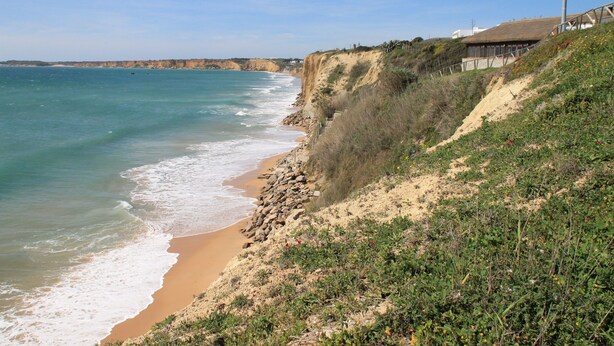 Eine Küstenlandschaft mit Sandstrand, Felsen und einem Gebäude mit einem Strohdach.