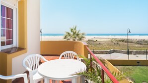 A balcony with a white table and chairs, overlooking a beach and ocean. - Beachfront apartment in Tarifa with pool (Tarifa)
