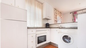 A compact kitchen with white cabinets, a built-in oven, a coffee maker, and a washing machine. - Beachfront apartment in Tarifa with pool (Tarifa)