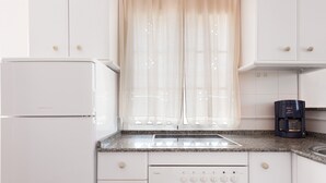 A kitchen with white cabinets, a built-in oven, a coffee maker, and a window with sheer curtains. - Beachfront apartment in Tarifa with pool (Tarifa)