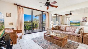 A living room with a sofa, coffee table, and chairs, a television, and a balcony with a view.