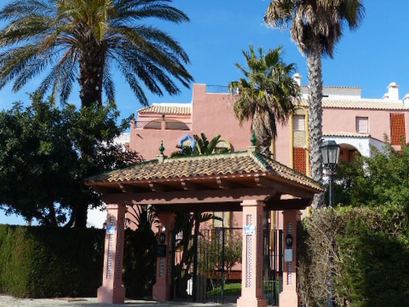 A traditional Spanish-style building with a tiled roof, a covered entrance, and palm trees in the background.