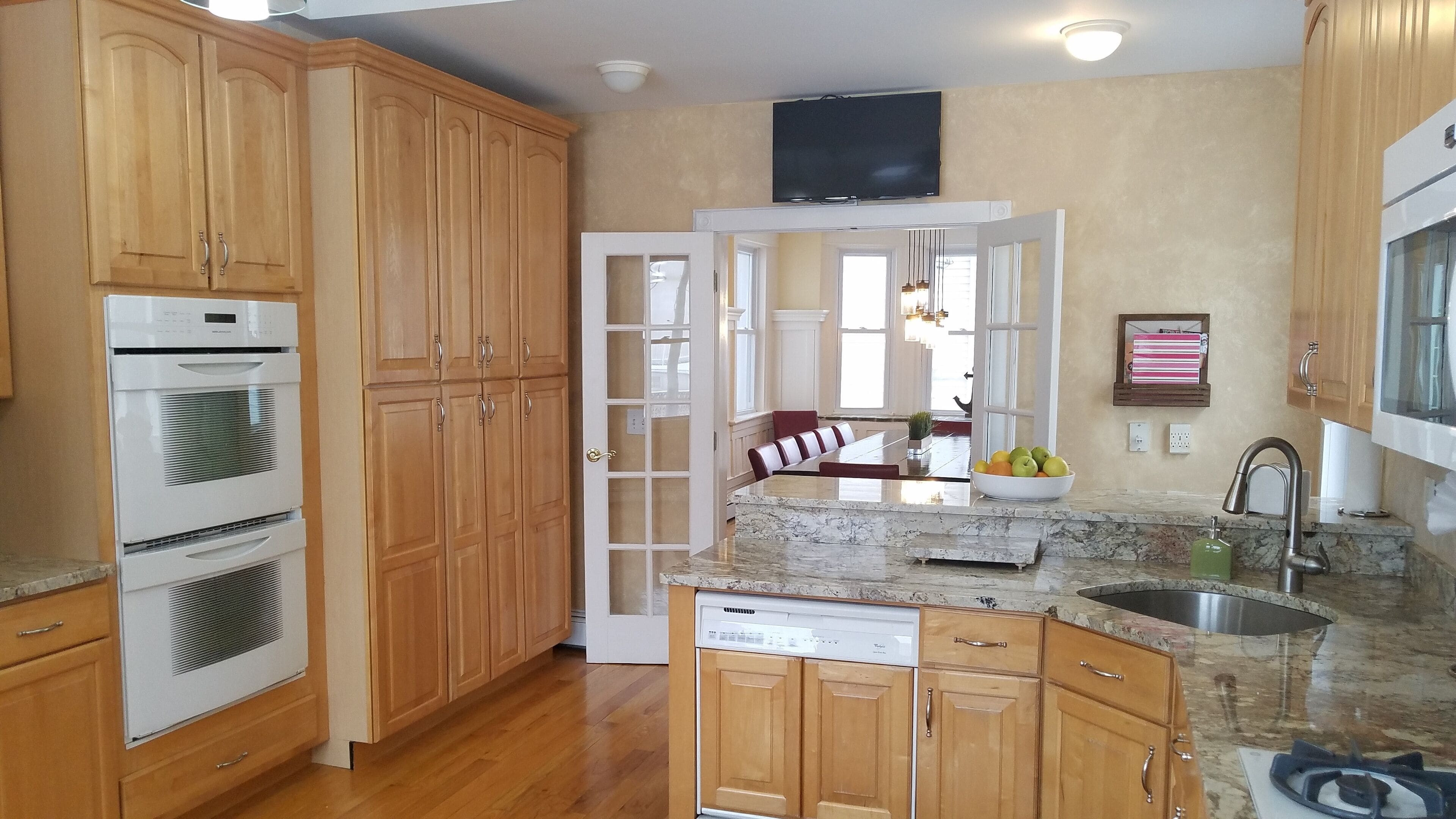A kitchen with wooden cabinets, a built-in oven, a dishwasher, a granite countertop, and a sink.