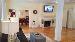 A living room with a fireplace, a television mounted on the wall, and a dining area in the background. - Beach Block 11 BDR Home (Ventnor City)