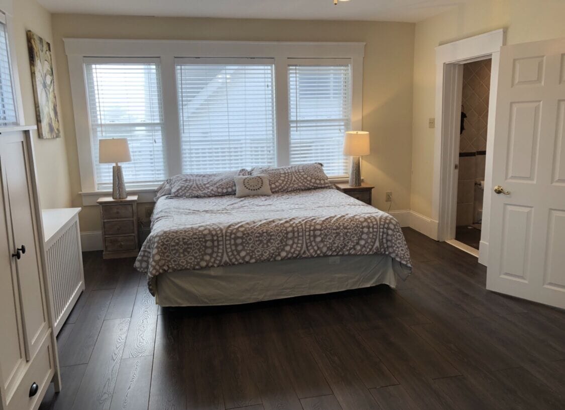 A bedroom with a large bed, two bedside tables with lamps, a radiator, and a door leading to another room.