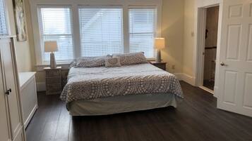 A bedroom with a large bed, two bedside tables with lamps, a radiator, and a door leading to another room.