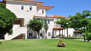 A two-story building with a red-tiled roof, a covered patio area, and a well-maintained lawn with a flower bed. - Independent condo, with stunning view just a heartbeat away from the beach (Kokkonion)