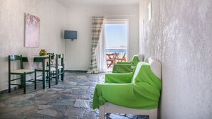 A room with a stone floor, a table with chairs, a green checkered sofa, a painting on the wall, and a view through a window with a curtain. - Independent condo, with stunning view just a heartbeat away from the beach (Kokkonion)