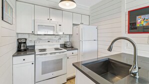 Cocina compacta con estufa, microondas, refrigerador y pileta con grifo moderno.