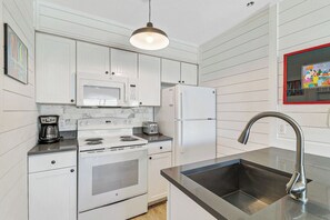 A compact kitchen with a stove, microwave, refrigerator, and a sink with a modern faucet.