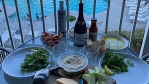 Una mesa con comida y bebidas en un balcón con vistas a una piscina y al océano.