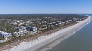 Vista aérea de una zona costera con una playa extensa, varios edificios de varios pisos y un cielo despejado.
