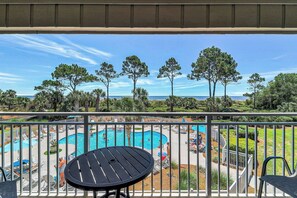Ein Balkon mit Blick auf ein Schwimmbad, Liegestühle und einen klaren Himmel.