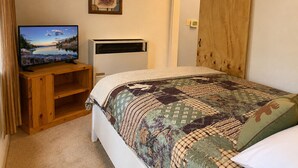 A bedroom with a bed, a television on a wooden stand, a heater, and a door.