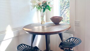 A dining area with a round table, two black chairs, a vase with flowers, and a bowl.