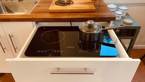 A kitchen with a built-in induction cooktop, a pot on it, and a wooden cutting board on the countertop.