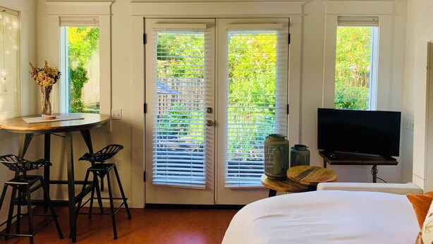 A bedroom with a bed, a TV, a desk with a chair, and a window with blinds.