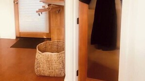 A room with a wooden floor, a closed door, a hanging coat rack, and a woven basket.