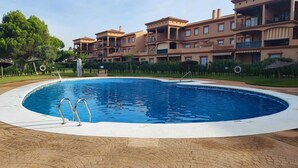 Una piscina rodeada por un patio de ladrillo, con un edificio de varios pisos al fondo.