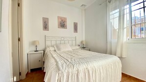 A bedroom with a bed, two bedside tables, and a window with curtains. - Beachfront apartment with large terrace (Tarifa)